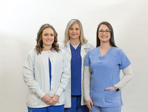 Picture three females smiling. There is one Physician and two Nurses.