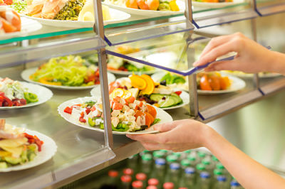 Picture of a buffet of several salads and a person opening a glass window that is a container over the salad bar / buffet to reach a salad out.