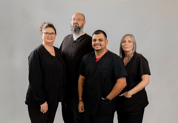 Picture of a female Radiology patient standing next to a Radiologist and a Radiologist Nurse. They are all smiling. There is a mammogram machine in the background.