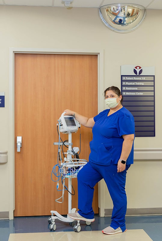 Picture of a female Nurse standing outside of patient hospital room, in front of the door.