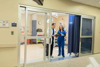 Picture of a male Physician and a female walking through emergency doors inside of the Hospital.